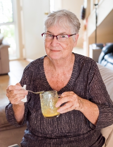 Older woman drinking a turmeric drink in her home - Australian Stock Image