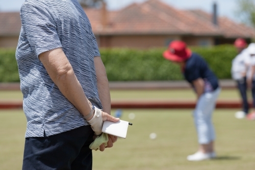 Older woman holding bowls scorecard behind her back - Australian Stock Image