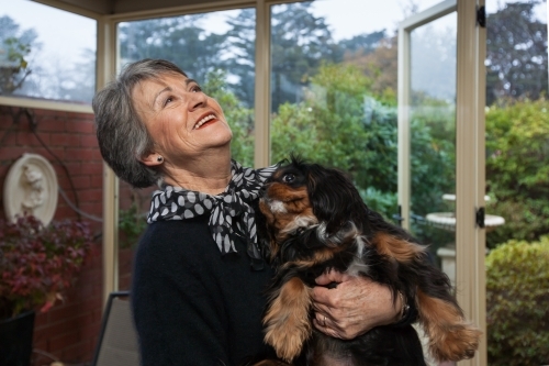 Older woman laughing while holding a small dog.