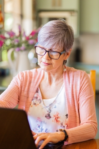Older woman using laptop computer at dining table - Australian Stock Image