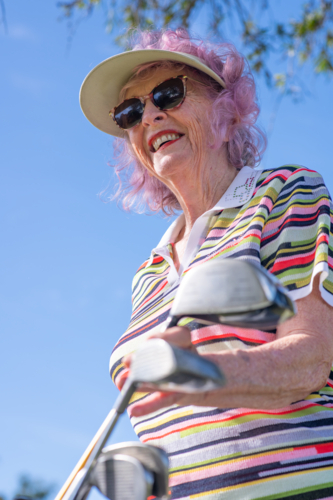 Older woman with pink hair wearing visor and striped shirt standing near golf clubs outdoors - Australian Stock Image