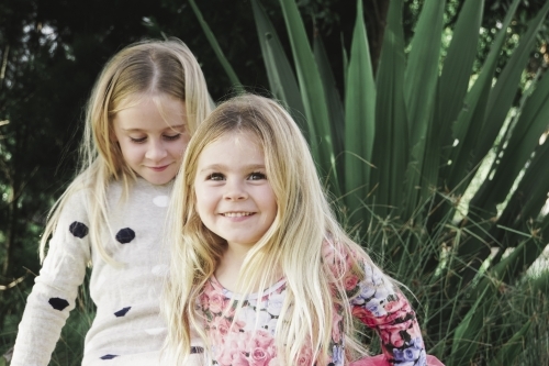 One girl looking down, one girl smiling while playing outdoors - Australian Stock Image