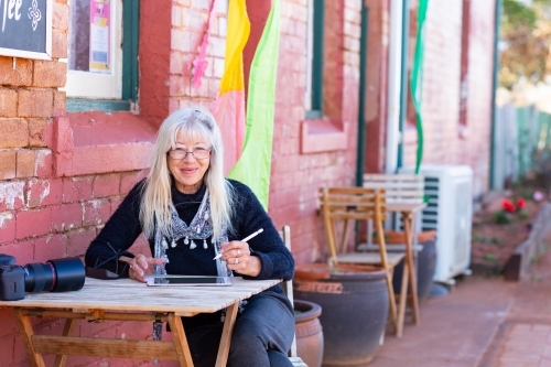one lady writing on digital tablet sitting at cafe table - Australian Stock Image
