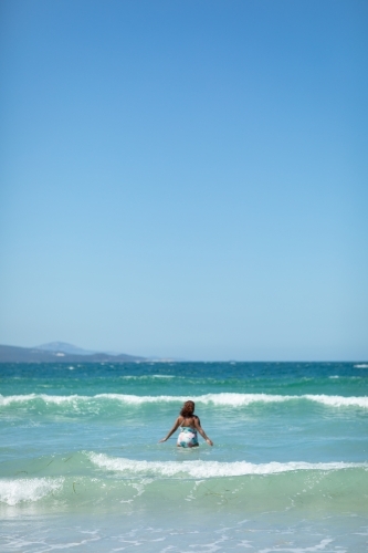 one person wading out into the waves at the beach - Australian Stock Image