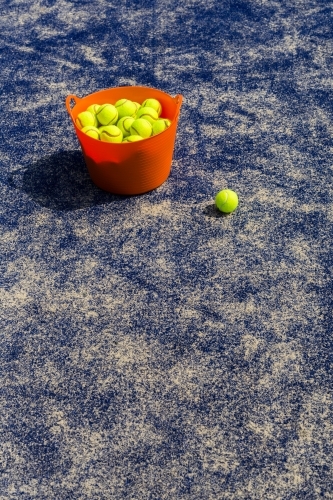 Orange basket of tennis balls on a blue tennis court