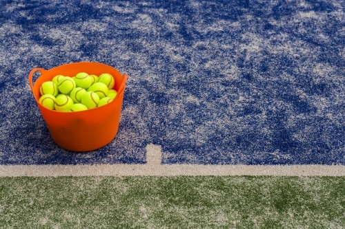 Orange basket of tennis balls on a blue tennis court