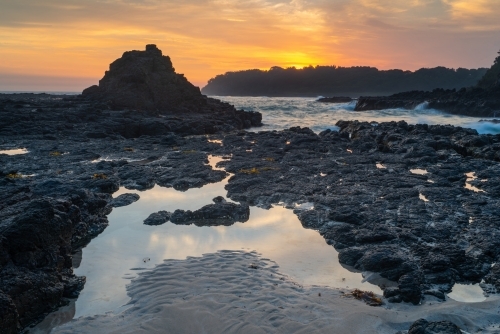 Orange clouds at dawn over rocks and ocean waves - Australian Stock Image