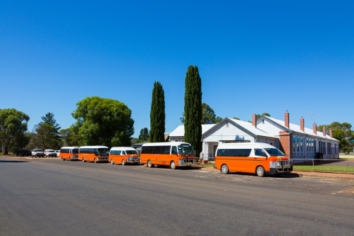 Orange school busses parked outside a small country school - Australian Stock Image