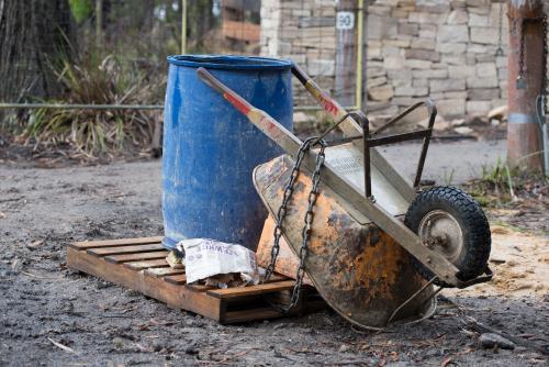 Orange wheelbarrow and blue barrel on wooden pallet in front of drystone wall - Australian Stock Image