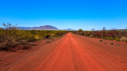 Outback red dirt road leading to mountains and blue sky - Australian Stock Image