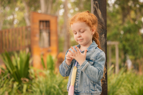Outdoor portrait of preschool age girl counting fingers on her hand at kindergarten - Australian Stock Image
