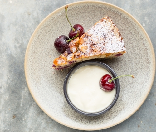 Overhead image single slice of cherry cake with icing dusting, cream and cherries on the side - Australian Stock Image