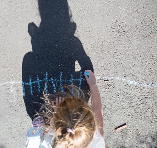 Overhead shadow of a young girl drawing with chalk on the road - Australian Stock Image