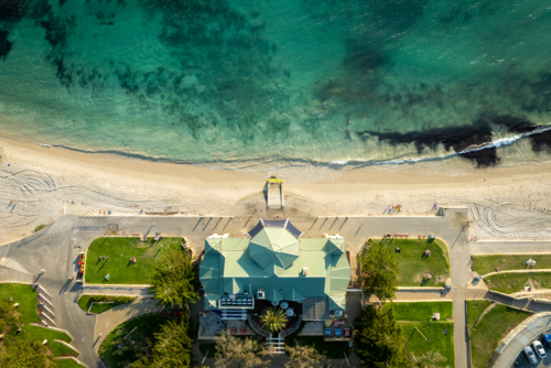 Overhead view of a green-roofed building and lawns next to a white sand beach. - Australian Stock Image