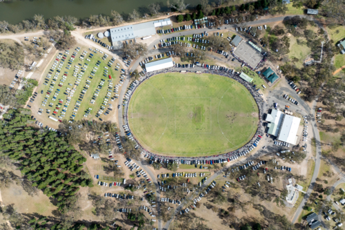 Overhead view of a rural football oval surrounded by parked cars and spectators. - Australian Stock Image