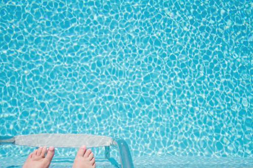 Overhead view of crystal blue swimming pool with toes and ladder at bottom edge of frame - Australian Stock Image