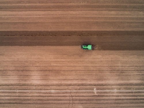 Overhead view of tractor on farm ploughing soil ready for planting new crop in fertile farmland - Australian Stock Image