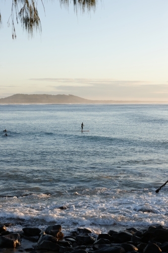Paddle boarder on wave at sunrise - Australian Stock Image