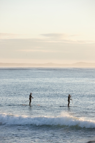 Paddle boarders on ocean at sunrise