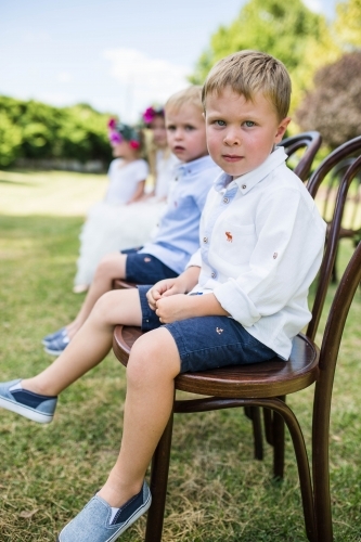Pageboys and flower girls sitting on chairs at wedding - Australian Stock Image