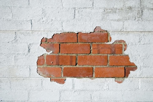 Paint peeling from a white wall showing red bricks
