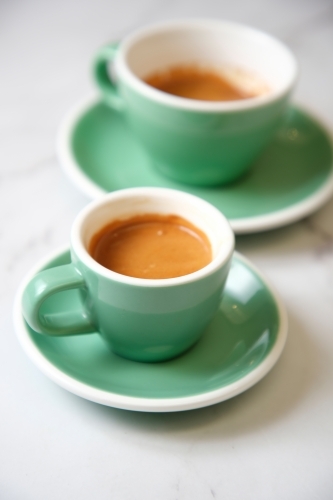 Pair of espressos in teal cup on marble table - Australian Stock Image