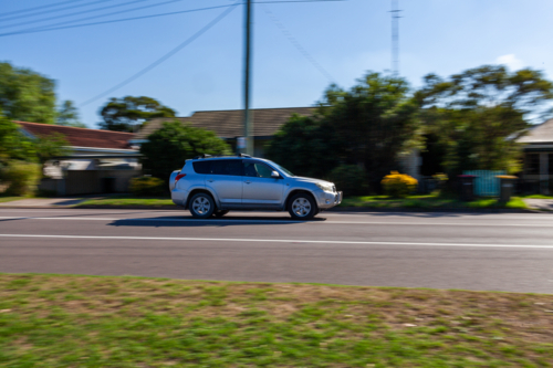 Panning shot of car vehicle traveling along highway through town - Australian Stock Image