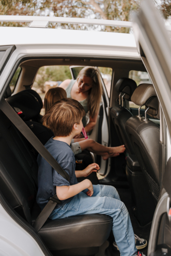 Parents helping the kids secure them in the car and booster seat. - Australian Stock Image