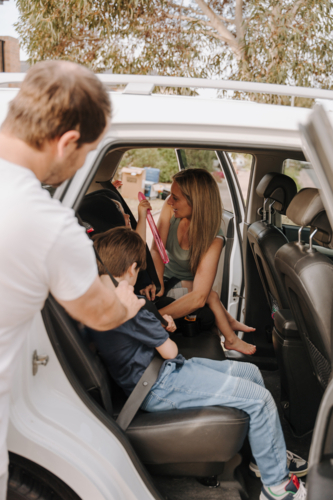 Parents helping the kids secure them in the car and booster seat. - Australian Stock Image