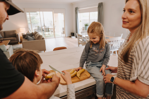 Parents teaching kids how to cut fruit in the kitchen - Australian Stock Image