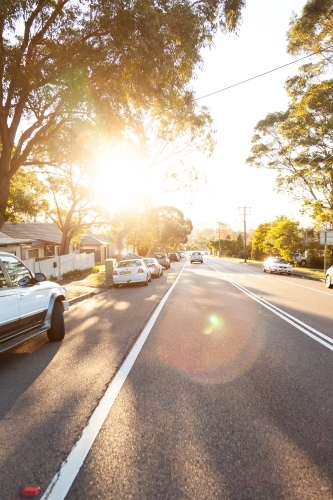 Parked cars on the side of a Newcastle road with sun flare through gum trees - Australian Stock Image