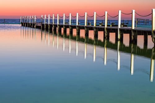 Pastel sunrise reflected off water at ocean baths Narrabeen