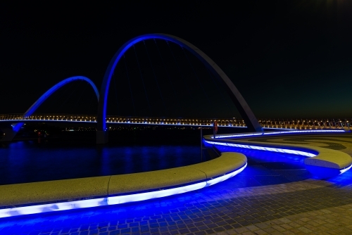 Path curving onto arched bridge with blue lighting and night sky - Australian Stock Image