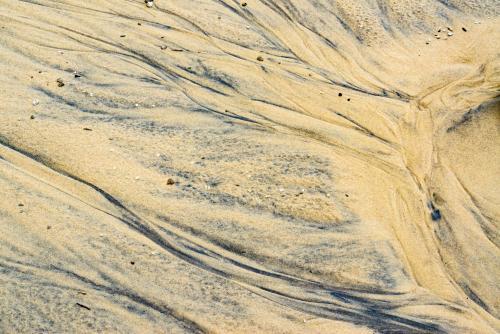 Patterns in wet yellow and black mineral sands on a beach at low tide - Australian Stock Image