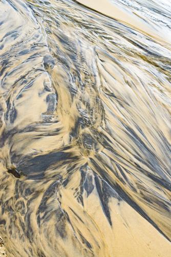 Patterns in wet yellow and black mineral sands on a beach at low tide - Australian Stock Image