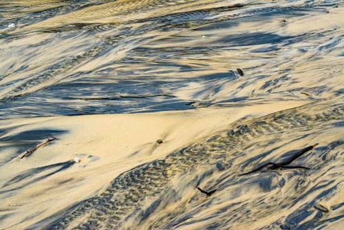 Patterns in wet yellow and black mineral sands on a beach at low tide - Australian Stock Image
