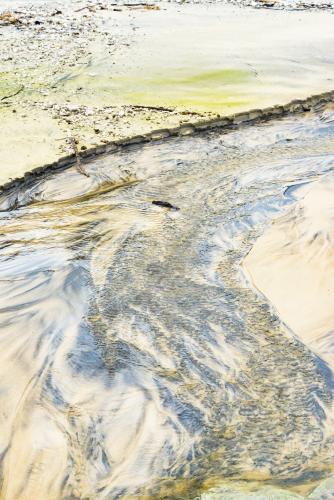Patterns in wet yellow and black mineral sands on a beach at low tide - Australian Stock Image