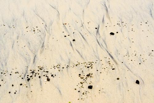 Patterns in wet yellow and black mineral sands on a beach at low tide with pebbles - Australian Stock Image
