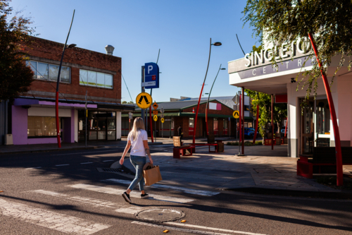 pedestrian crossing road holding brown shopping bag in urban area of singleton - Australian Stock Image