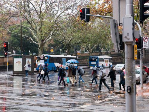 Pedestrians with umbrellas crossing at traffic lights on a rainy day - Australian Stock Image
