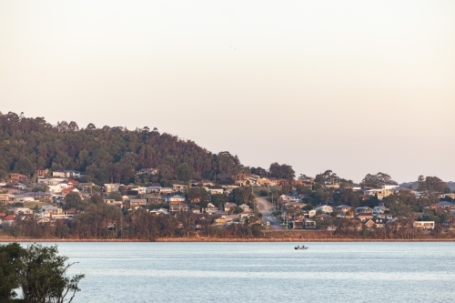 People fishing in boat on Lake Macquarie with houses on hill in background - Australian Stock Image