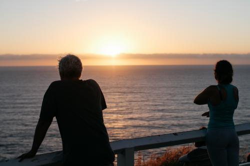 People in silhouette watching the sunrise over water - Australian Stock Image