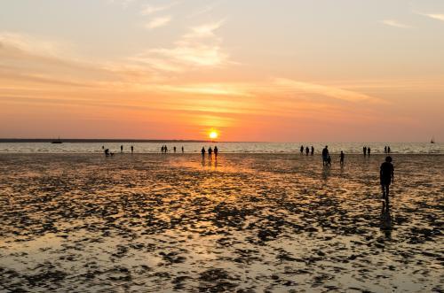 People like to walk out on the tidal flats in the colourful sunset at Menindee Beach - Australian Stock Image