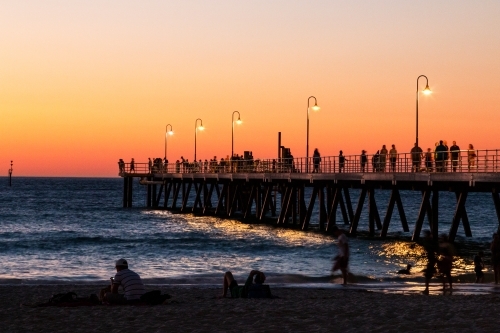people on beach and jetty at sunset - Australian Stock Image