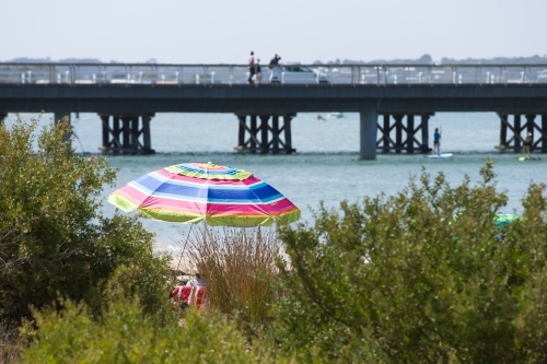 People relaxing under a beach umbrella with bridge in background - Australian Stock Image