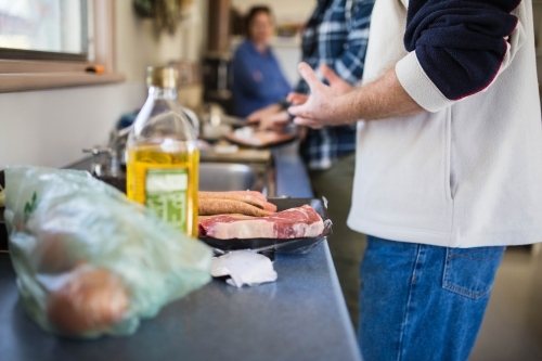 People standing near kitchen sink helping prepare food for lunch - Australian Stock Image