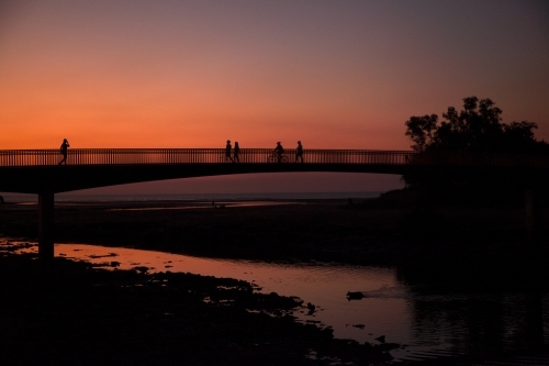 People walking across bridge at sunset - Australian Stock Image