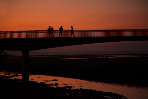 People walking across bridge at sunset - Australian Stock Image