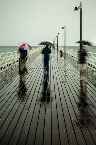 People walking on a pier with umbrellas on a rainy day.