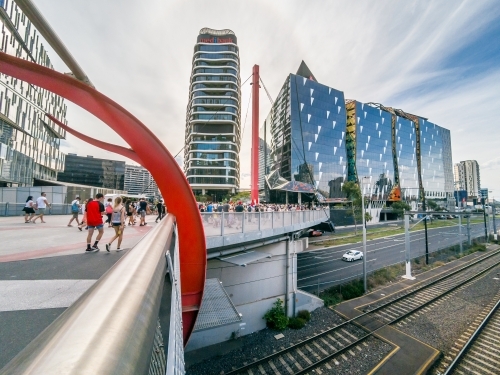People walking on a transit bridge over roads and railway lines towards city buildings